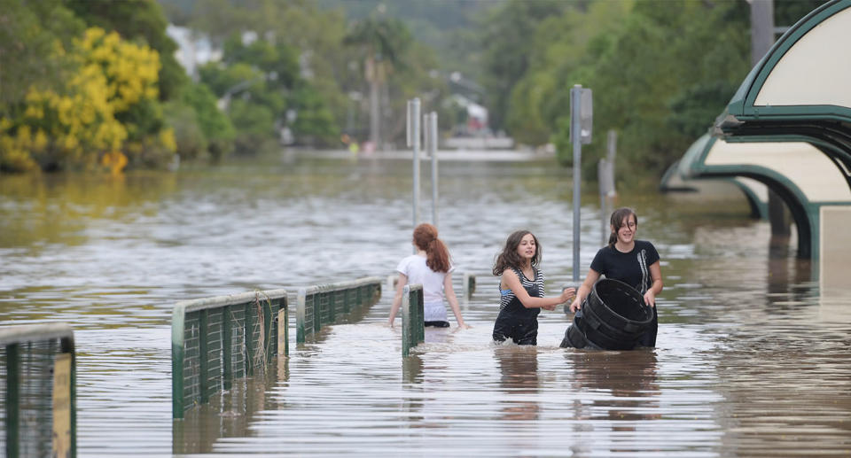 Three girls collecting belongings while walking through flood waters. Source AAP