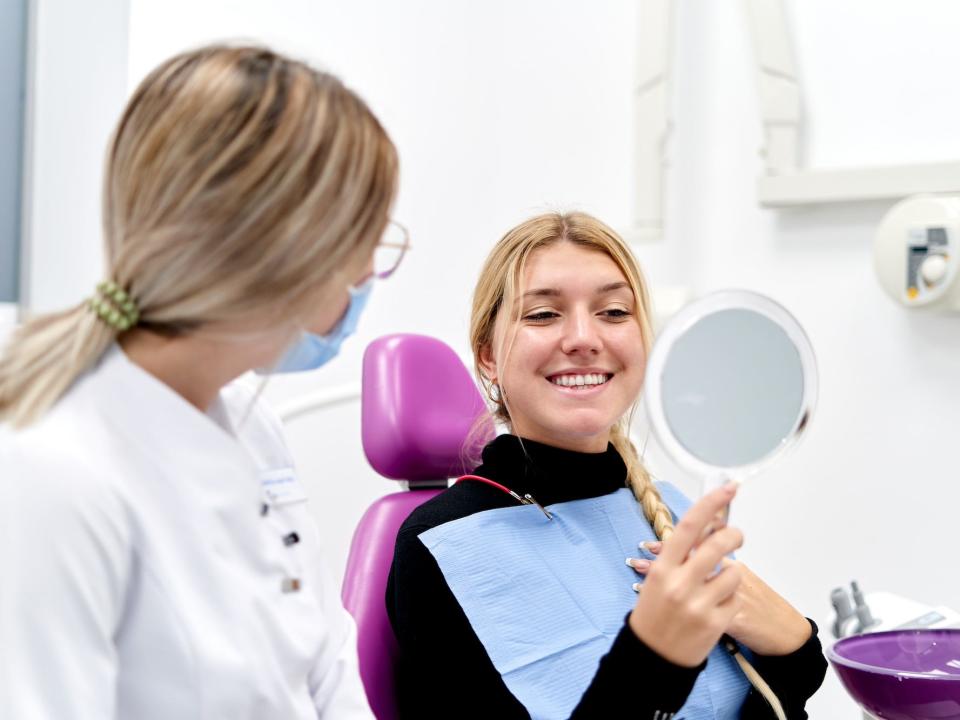 Patient looking at her teeth in a mirror and next to her is a dentist or a worker in a dental office