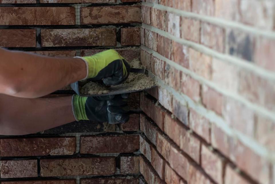 A close up of a worker's hands repairing a brick wall.