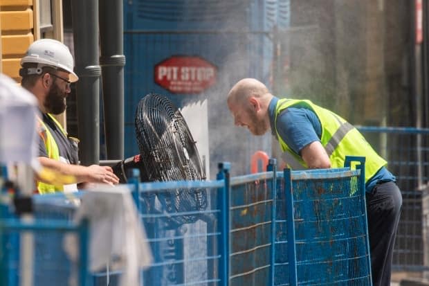 A construction worker uses a misting fan to cool down at a work site in Vancouver on June 28, amid a record heat wave in B.C. (Ben Nelms/CBC - image credit)