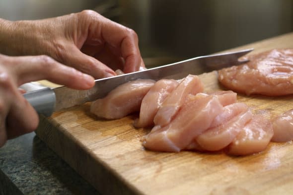 'image of raw chicken being sliced, there is motion blur in the hands and the knife, shallow depth of field.more kitchen and foo