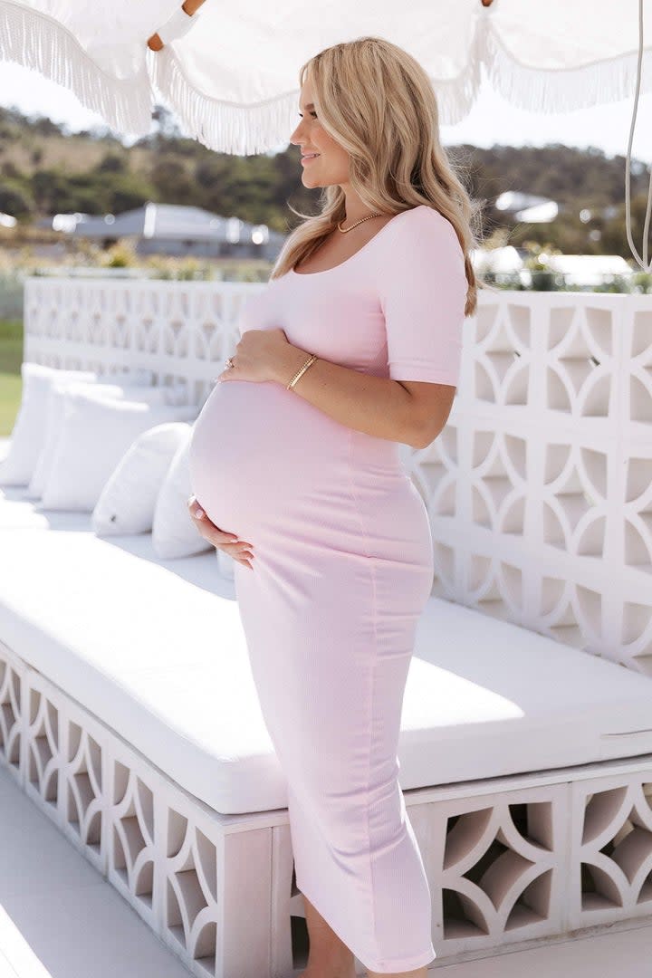 A woman wears a pink Sorella dress, $69.95, from Petal & Pup, with scoop neck and short sleeves. It is below calf length.