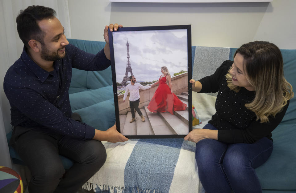 Celso Franco Junior and wife Juliana Franco pose for photos holding a photograph of themselves in Paris, in Suzano, greater Sao Paulo area, Brazil, Tuesday, May 25, 2021. The couple have lined their nest in Suzano, a commuter city near Sao Paulo, with trinkets that recall the time before Brazil became a no-go zone for foreign travel, red-listed internationally because of the contagious variant that first ravaged the Amazon city of Manaus. (AP Photo/Andre Penner)