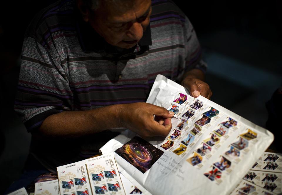 Herman Sanchez pastes a stamp of Britain's Ben Ainslie collected during the 2012 Summer Olympics on Wednesday, Aug. 8, 2012, in London. London has been issuing stamps every day with photos of Britain’s gold medallists. (AP Photo/Emilio Morenatti)