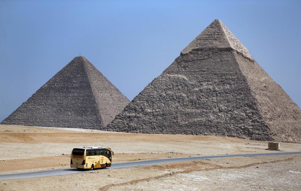 In this Saturday, Sept. 7, 2013 photo, a tour bus passes near the historical site of the Giza Pyramids, near Cairo, Egypt. Before the 2011 revolution that started Egypt's political roller coaster, sites like the pyramids were often overcrowded with visitors and vendors, but after a summer of coup, protests and massacres, most tourist attractions are virtually deserted to the point of being serene. (AP Photo/Lefteris Pitarakis)