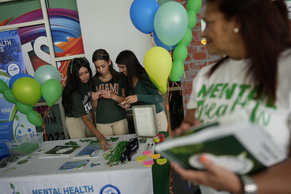 Members of the Miami Arts Studio mental health club, including from left, Salet Aquino, Dominique Rodriguez, and club president Anaeli Souto, man a table as they raise awareness on World Mental Health Day, Tuesday, Oct. 10, 2023, at Miami Arts Studio, a public 6th-12th grade magnet school, in Miami. (AP Photo/Rebecca Blackwell)