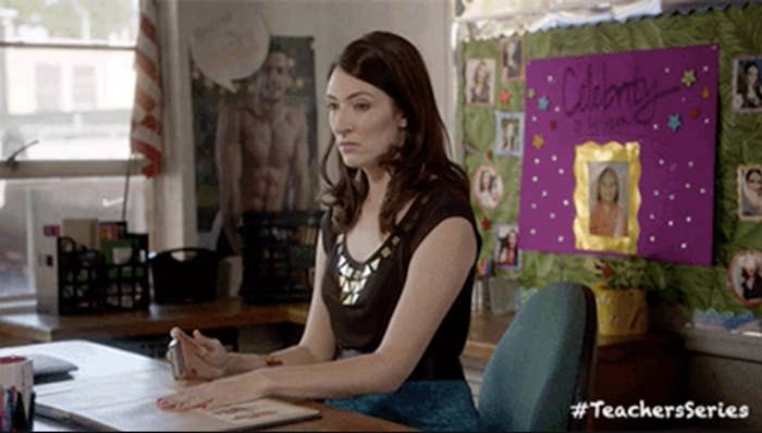 Woman seated at a desk with posters and a "#TeachersSeries" hashtag on the wall