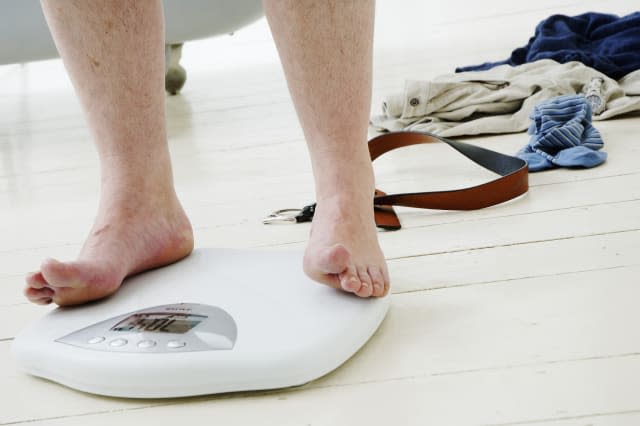 Man standing on scales by clothes and belt, low section, close-up