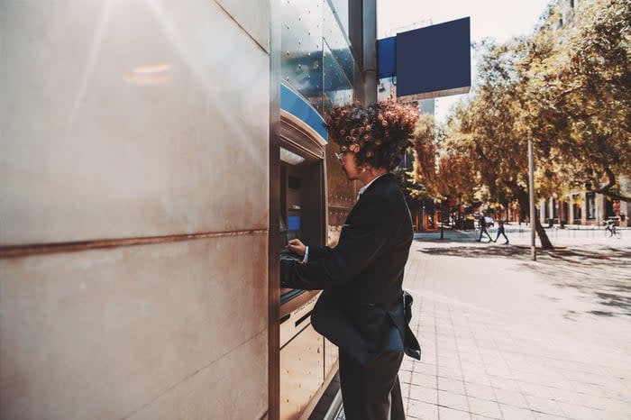 A young man in a suit using an outdoor ATM.