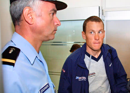FILE PHOTO: U.S. Postal Service team leader Lance Armstrong (R) of the USA looks at a French gendarme before boarding the plane which takes the riders from Grenoble to Perpignan for the transfer stage of the Tour de France cycling race in Grenoble, France, July 19, 2001. REUTERS/Pool/File Photo