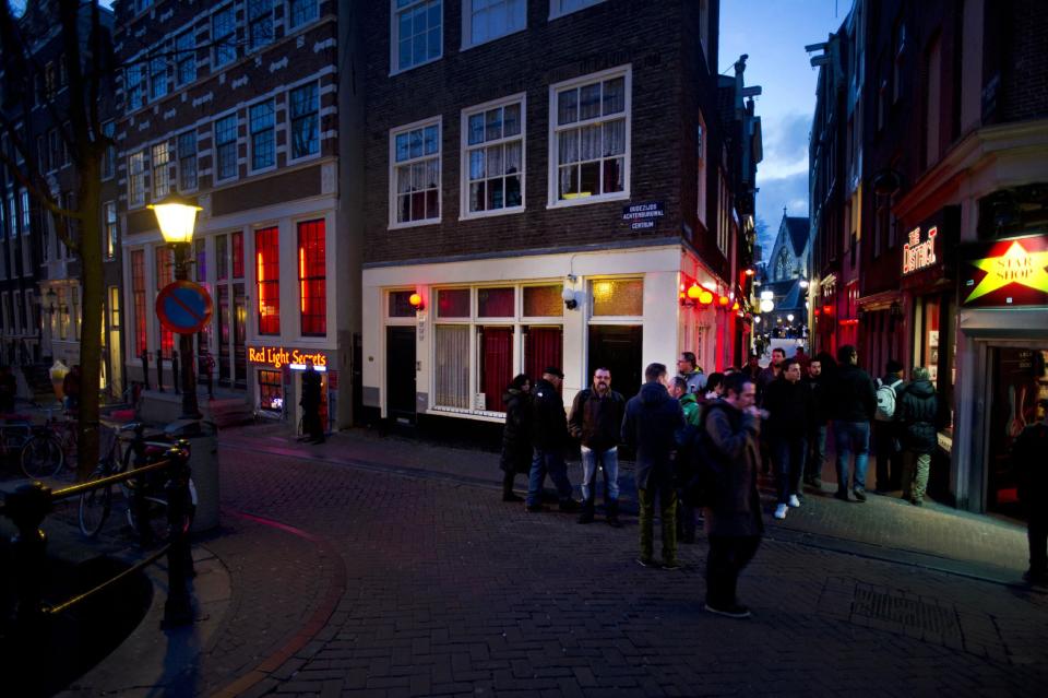 In this photo taken Tuesday, Feb. 4, 2014, tourists pack the narrow streets of Amsterdam’s famed Red Light District near the entrance of the 'Red Light Secrets' museum, left, in Amsterdam. On any given evening, thousands of tourists visit Amsterdam's famed Red Light District, gawking at ladies in lingerie who work behind windows, making a living selling sex for money. Now a small educational museum is opening in heart of the district that aims to show reality from the other side of the glass. Organizer Melcher de Wind says the Red Light Secrets museum is for those who want to learn more about how the area works without actually visiting a prostitute. (AP Photo/Evert Elzinga)