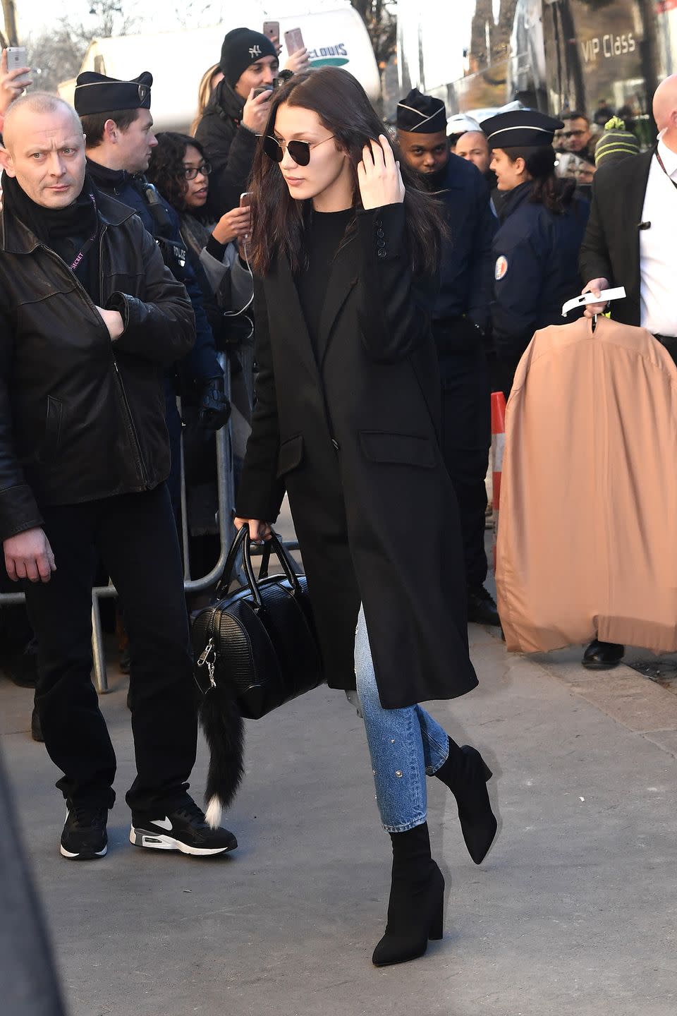 <p>In a black peacoat, black top, studded light wash jeans, black sock boots, a leather handbag and cat eyed sunglasses. </p>