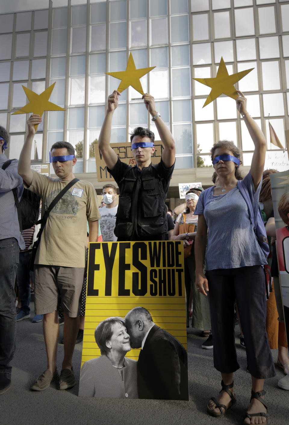 Protesters hold European Union stars and keep their eyes closed behind a poster showing German Chancellor Angela Merkel and Bulgarian Prime Minister Boyko Borissov in front of the German Embassy in Sofia, Bulgaria, Wednesday, Aug. 12, 2020. Several hundred anti-government protesters gathered on Wednesday in front of Germany’s embassy in Sofia, calling on Berlin and Brussels to “open their eyes” to widespread corruption in Bulgaria. During the peaceful protest, dubbed “Eyes Wide Shut,” organizers complained that the European Union has willfully ignored the state of affairs in its poorest member state. (AP Photo/Valentina Petrova)