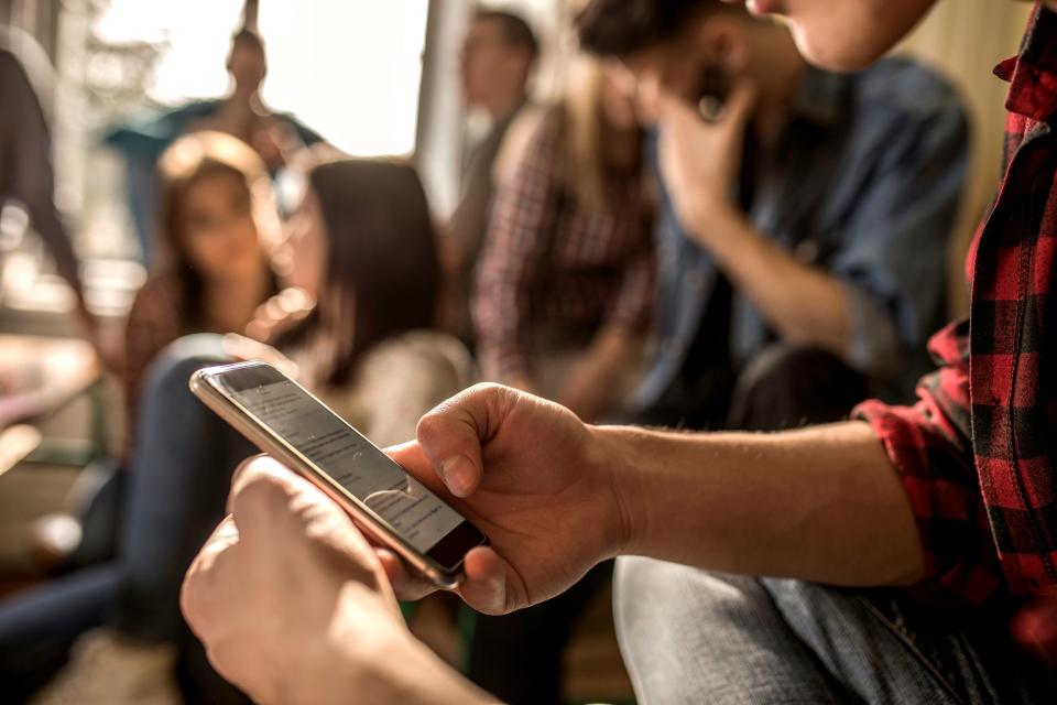 Unrecognizable male student text messaging on mobile phone while being on a break in the classroom.