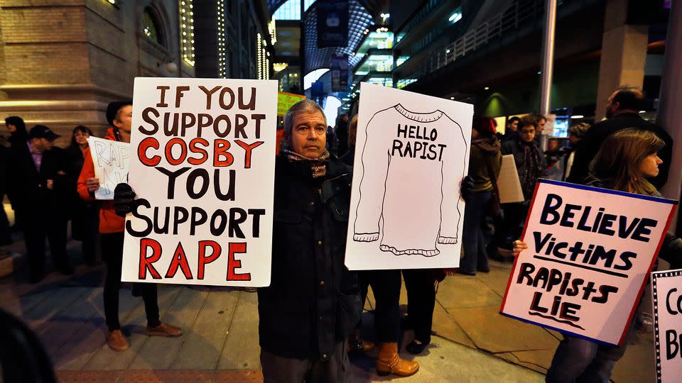 Demonstrators hold signs protesting a performance underway by comedian Bill Cosby inside the Buell Theater in Denver. Photo: AP Photo/Brennan Linsley