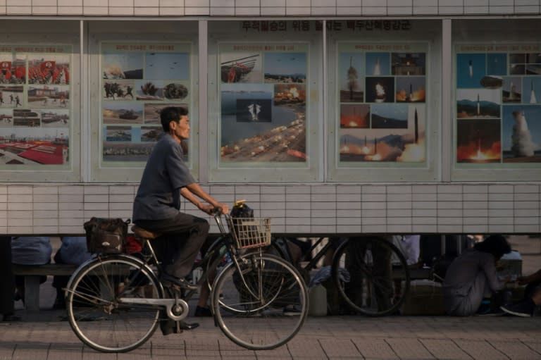 A cyclist passes a display featuring images of missile launches and military exercises on a street in Pyongyang