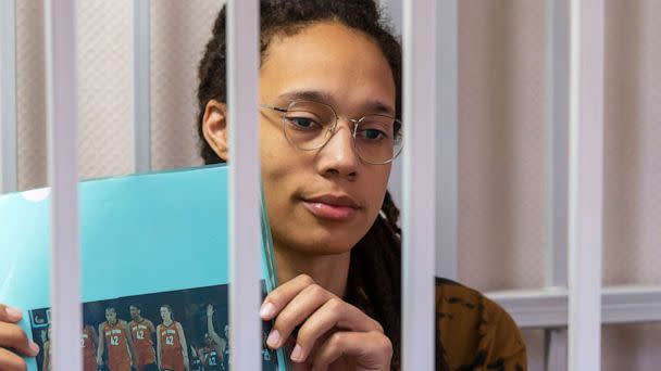 PHOTO: WNBA star and two-time Olympic gold medalist Brittney Griner holds up a photo of players from the recent all star game wearing her number, sitting in a cage at a court room prior to a hearing in the Khimki district court, July 15, 2022. (Dmitry Serebryakov/AP)