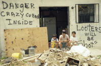 <p>Orlando Somante, center, sits with his sons Orlando, left, and Jonathan, right, amid the rubble of their home in Cutler Ridge, with signs that warn “Looters Will be Shot”, and “Danger, Crazy Cuban Inside”, Aug. 27, 1992. Their home was one of many in South Dade County that was hit by Hurricane Andrew last Monday. (AP Photo/Gaston de Cardenas) </p>