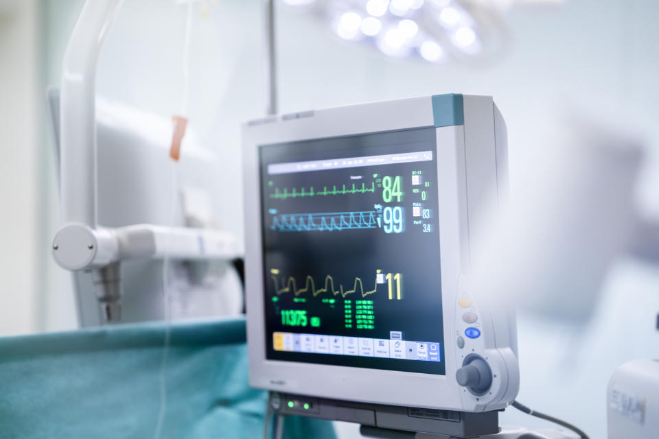 A hospital monitor displays vital signs including heart rate, blood oxygen levels, and other medical data in an operating room