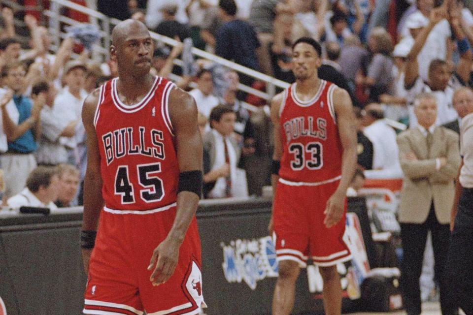 Two men in red basketball uniforms walk along the sidelines.