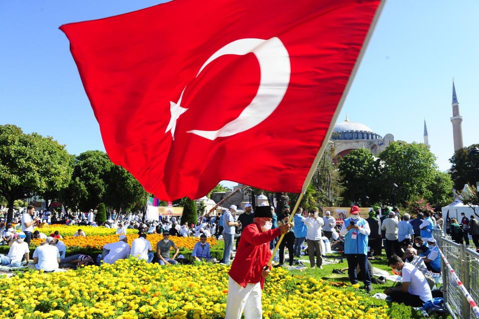 A man waves a Turkish flag outside the Byzantine-era Hagia Sophia, in the historic Sultanahmet district of Istanbul, Friday, July 24, 2020. Hundreds of Muslim faithful were making their way to Istanbul's landmark monument Friday to take part in the first prayers in 86 years at the structure that was once Christendom's most significant cathedral and the "jewel" of the Byzantine Empire then a mosque and museum before its re-conversion into a Muslim place of worship. The conversion of the edifice, has led to an international outcry. (AP Photo/Omer Kuscu)