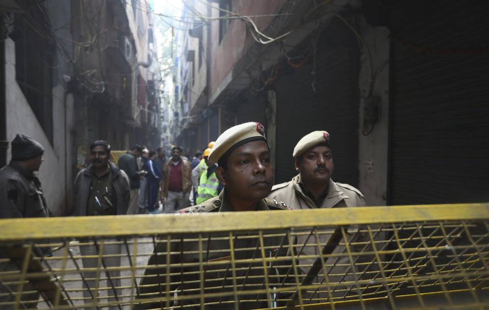 Policemen and neighbors stand in front of a ilnl-fated building which caught fire on Sunday, in New Delhi, India, Monday, Dec. 9, 2019. Authorities say an electrical short circuit appears to have caused a devastating fire that killed dozens of people in a crowded market area in central New Delhi. Firefighters fought the blaze from 100 yards away because it broke out in one of the area's many alleyways, tangled in electrical wire and too narrow for vehicles to access. (AP Photo/Manish Swarup)