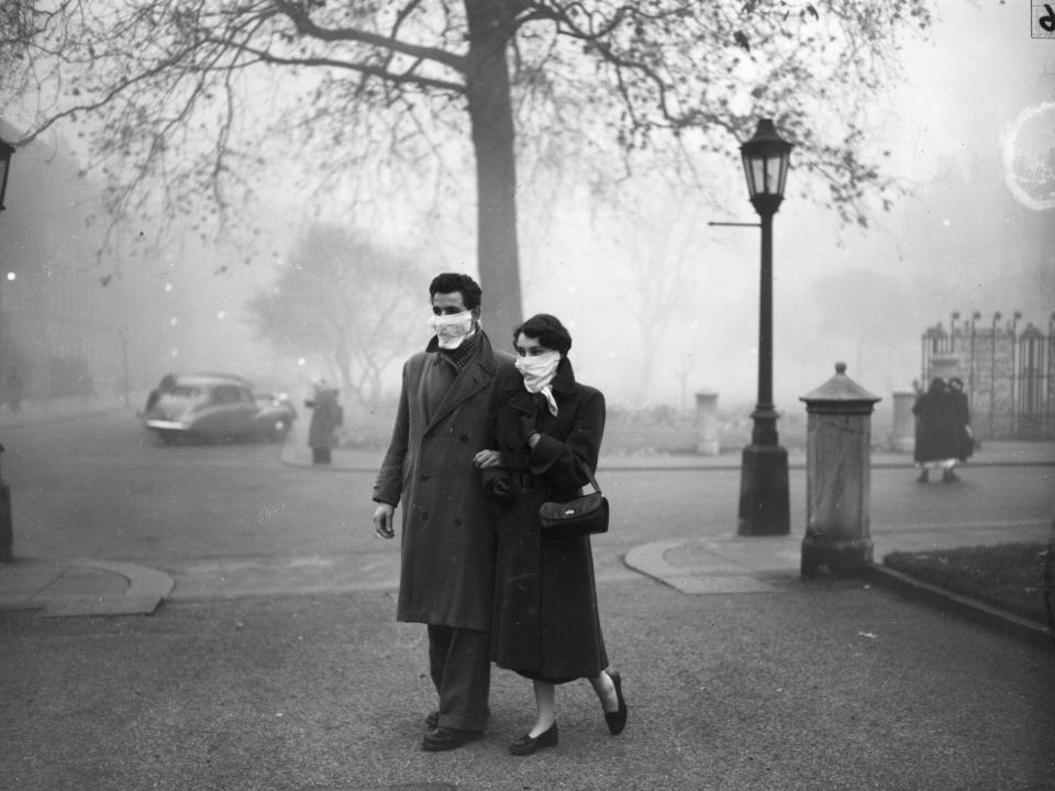 A couple walking in London wearing smog masks on a foggy day in 1953.