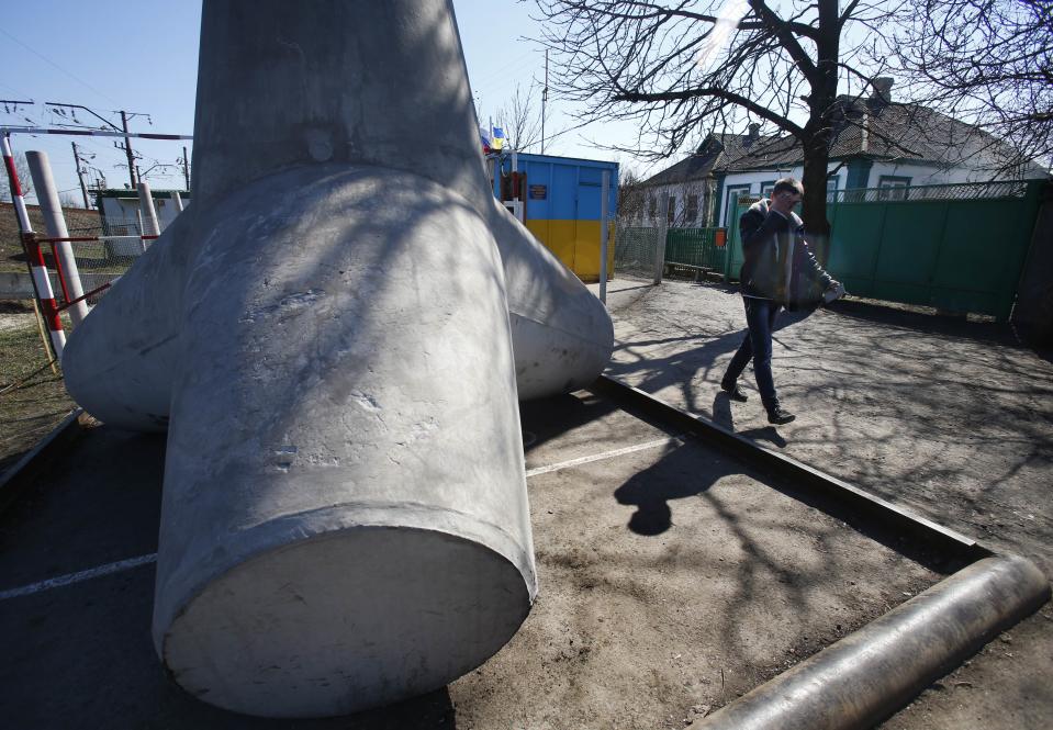 In this photo taken Monday, March 24, 2014, a man walks past a concrete block placed to limit traffic at the border crossing between Ukraine and Russia in the village of Vyselki, eastern Ukraine. Ever since the 1991 breakup of the Soviet Union, the village of Vyselki has been split between Ukraine and Russia. For years its residents have continued to live together peacefully, doing most of their shopping in one country and paying their electricity bills in another. But after Russia seized the Crimean Peninsula from Ukraine, the Ukrainian villagers fear a further incursion of Russian troops, while the Russians say they would welcome their protection against the new pro-Western government in Kiev. (AP Photo/Sergei Grits)