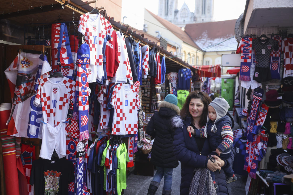 A woman carrying her child walks among shops selling Croatian football jerseys and various fan props, prior to the Qatar World Cup semi-final match between Croatia and Argentina, in Zagreb, Croatia, Tuesday, Dec. 13, 2022. (AP Photo/Armin Durgut)