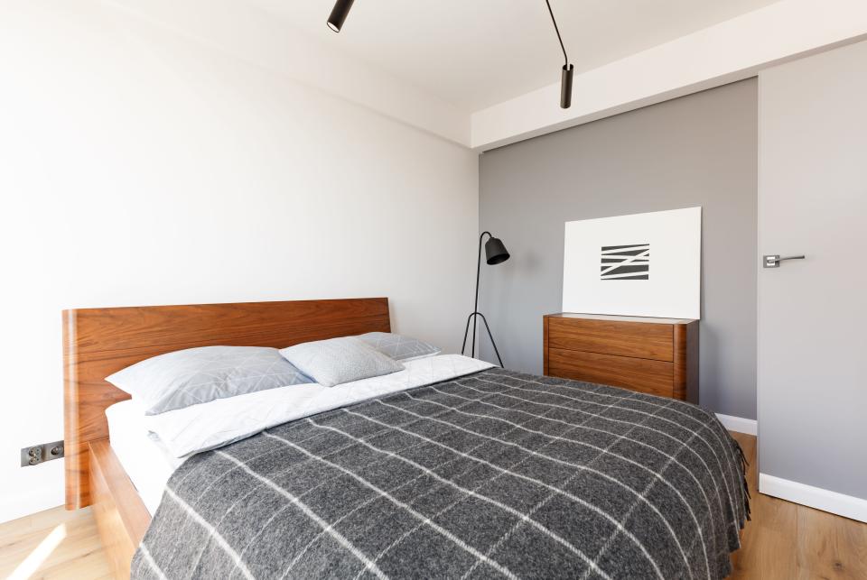 A simple-looking bedroom with a double bed with a wooden headboard and a matching cabinet up against a grey feature wall.