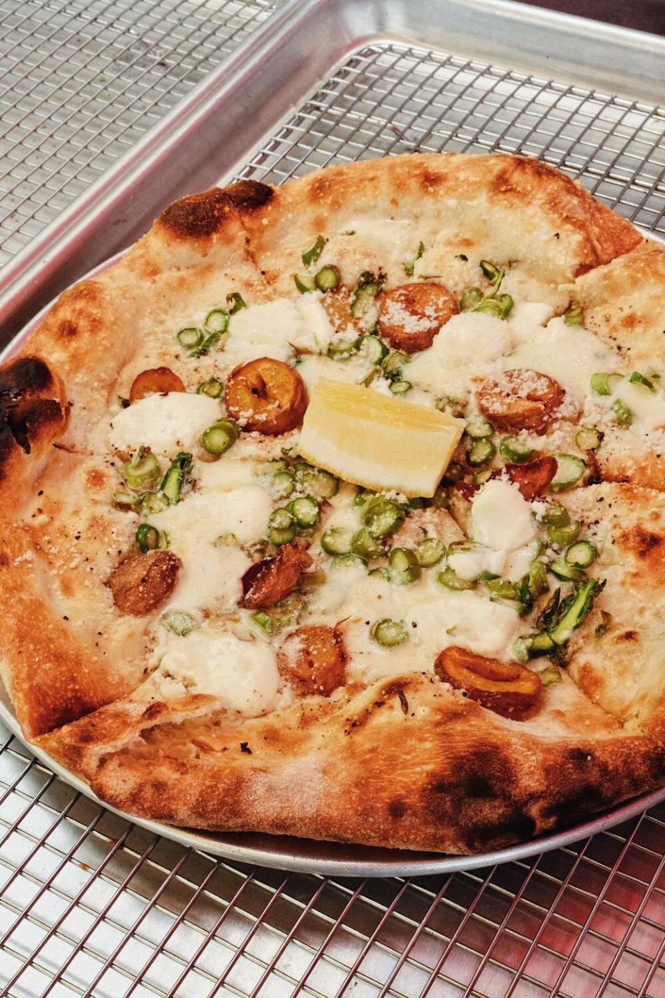 A vertical close-up of an asparagus pizza on a silver baking tray at Fiorelli Pizza at the Cook's Garden in Venice.