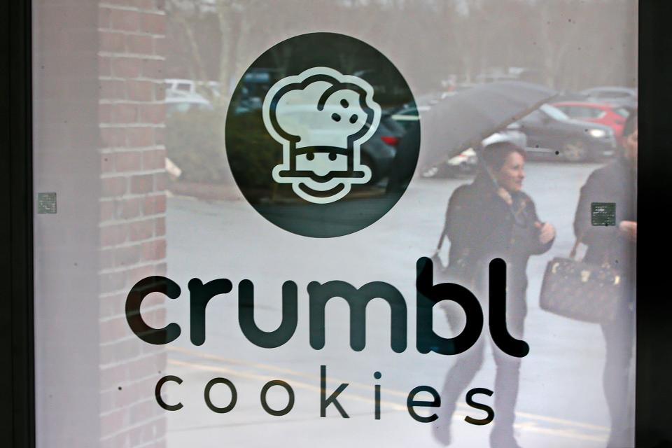 A woman with an umbrella is reflected off of the glass door of the future Crumbl Cookies to open next to TJ Maxx in Dartmouth.