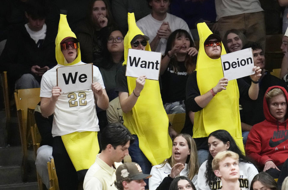 Fans dressed as bananas hold up a sequence of signs in hopes that Jackson State head football coach Deion Sanders will take the head coach opening at Colorado in the second half of an NCAA college basketball game as Colorado hosts Arizona State, Thursday, Dec. 1, 2022, in Boulder, Colo. (AP Photo/David Zalubowski)