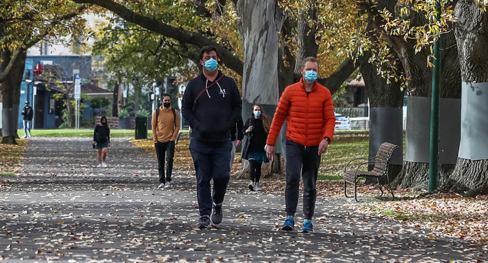 People with face masks walk through a park in Melbourne during Covid lockdown.