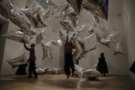 Tate representatives pose for photographs by interacting with the Andy Warhol piece "Silver Clouds" 1966, reprint 1994 helium-filled metalised plastic film (Scotchpak) during a media preview for the exhibition "Andy Warhol" at the Tate Modern gallery in London, Tuesday, March 10, 2020. The exhibition, which runs from March 12 to September 6, features over 100 works spanning the American artist's career in the second half of the 20th century until his death in 1987. (AP Photo/Matt Dunham)