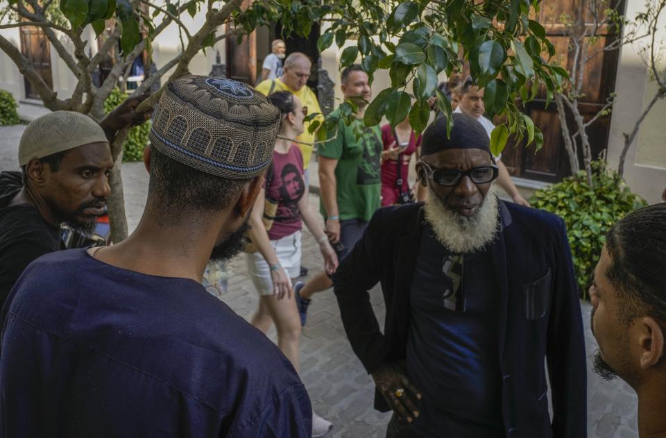 Varios musulmanes hablan frente a su mezquita mientras un grupo de turistas --algunos de ellos con camisetas que llevan la imagen del revolucionario cubano Ernesto "Che" Guevara-- pasan a un costado, el viernes 16 de febrero de 2024, en La Habana, Cuba. La única mezquita de la capital cubana abrió sus puertas en 2015, y la comunidad musulmana suma ahora unas 2.500 personas en todo el país. (AP Foto/Ramón Espinosa)