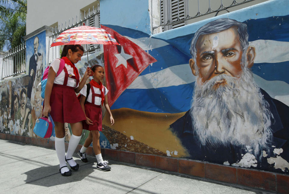 In this photo taken Monday April 23, 2012, primary school students walk past a mural depicting heros of Cuba's independence from Spain, including Cuban patriot Francisco Vicente Aguilera, right, who later supported Carlos Manuel de Cespedes in the revolt against Spain, in Bayamo, a colonial town in Oriente province. The color of children's uniforms denotes their educational level. (AP Photo/Kathy Willens)