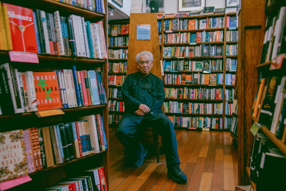 An older man seated in the middle of a large bookstore.