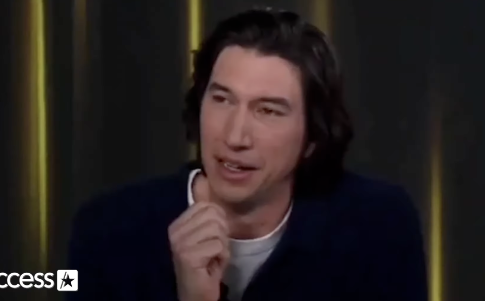 Adam Driver speaking during an interview on Access with a thoughtful expression, wearing a casual dark shirt