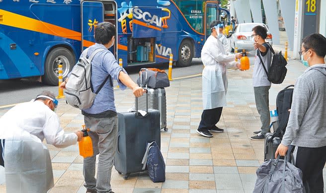 搭乘日本航空自印度返台的旅客，8日中午抵達台北松山機場，經防疫人員協助消毒後，乘坐遊覽車前往集中檢疫所。（姚志平攝）