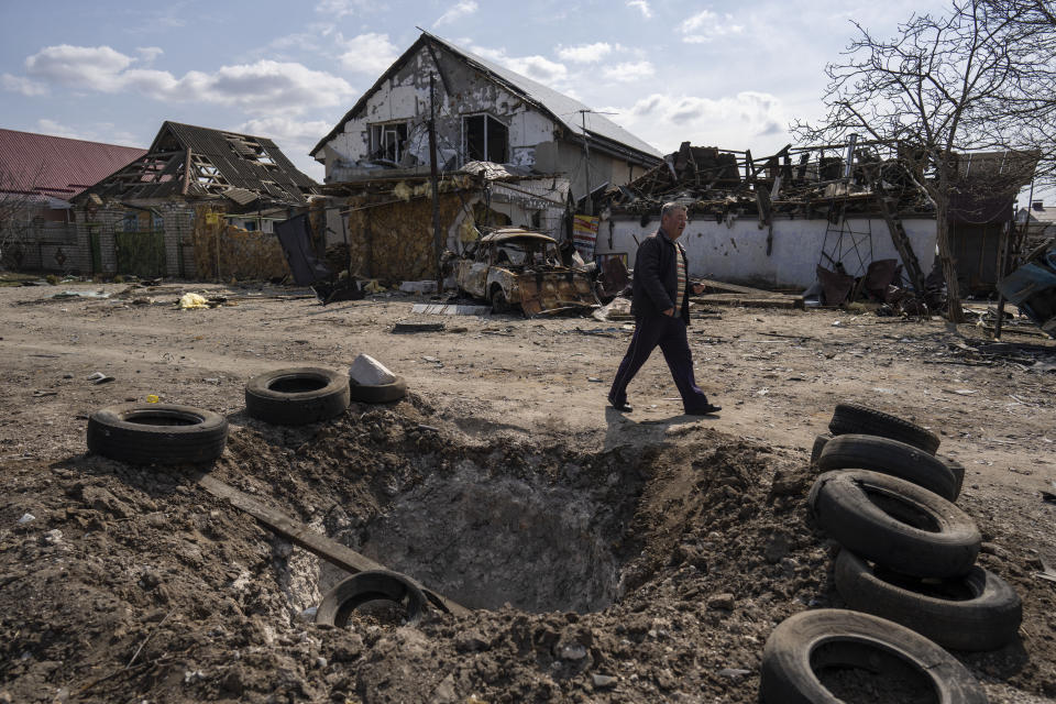 FILE - A man walks behind a crater created by a bomb and in front of damaged houses following a Russian bombing earlier this week, outskirts Mykolaiv, Ukraine, Friday, 25, 2022. With its aspirations for a quick victory dashed by a stiff Ukrainian resistance, Russia has increasingly focused on grinding down Ukraine’s military in the east in the hope of forcing Kyiv into surrendering part of the country’s eastern territory to end the war. If Russia succeeds in encircling and destroying the Ukrainian forces in Donbas, the country’s industrial heartland, it could try to dictate its terms to Kyiv -- and possibly attempt to split the country in two. (AP Photo/Petros Giannakouris)