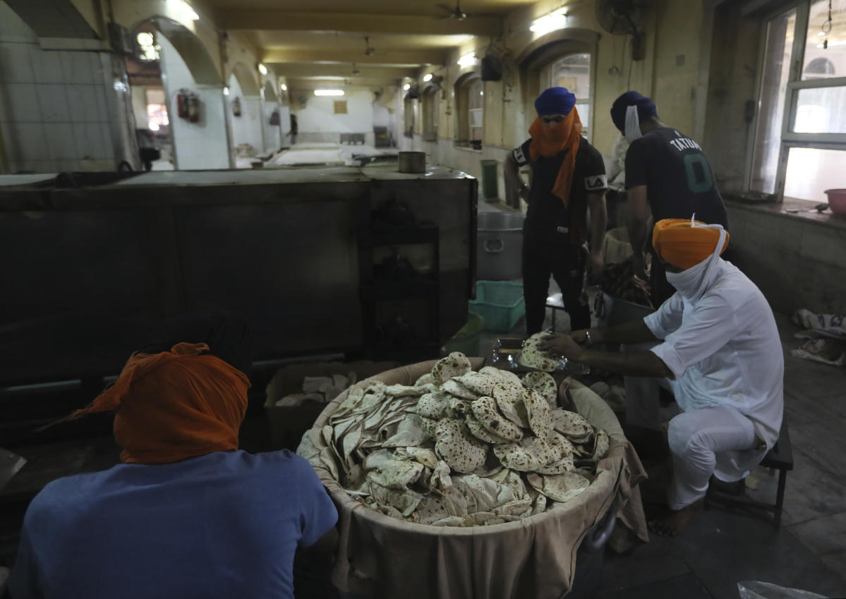 A cook in a Sikh kitchen cooking in an extremely large pot.