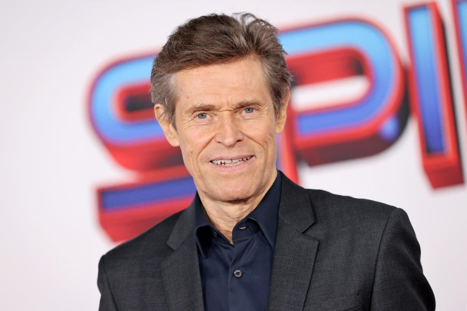 Willem smiling, wearing a black suit jacket with a navy shirt underneath