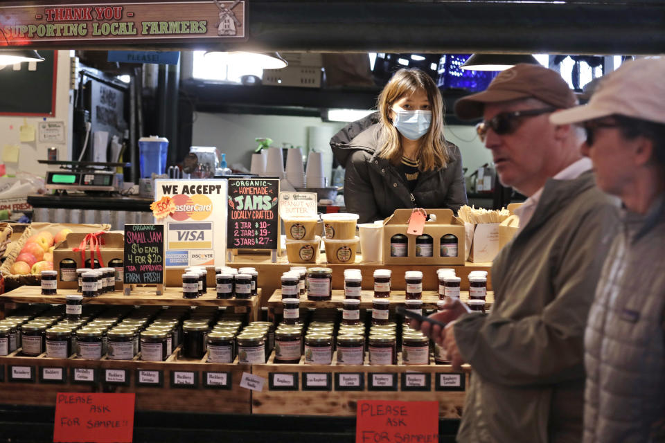 Vendor Belle Naing watches people walk past her jam and produce stand at the Pike Place Market, Friday, March 20, 2020, in Seattle. Many shops in the landmark market, including fish, meat, bakeries and produce grocers, continue to remain open, though business has dropped considerably in recent weeks. Restaurants, except for take-out orders, are closed, workers who can are working from home and people are being asked to maintain physical distance from others to help stop the spread of COVID-19. Washington state health officials reported eight new coronavirus deaths on Friday, bringing the total to 83. Seven of those deaths were in King County, the epicenter of the outbreak in the state. (AP Photo/Elaine Thompson)