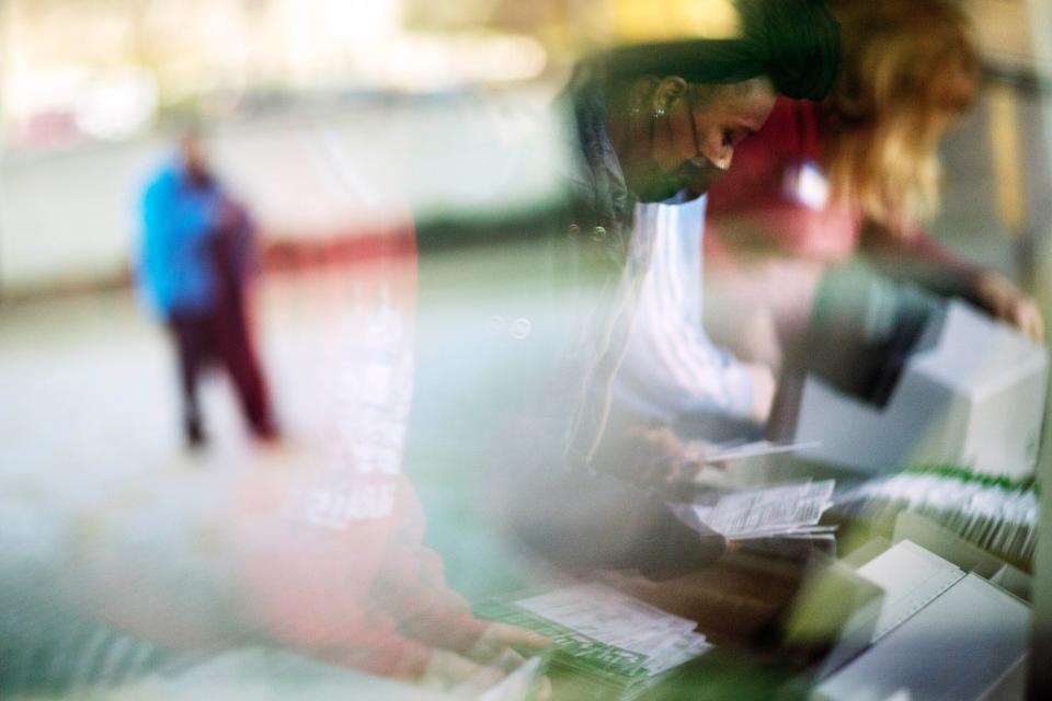 In this Nov. 3 photo, election inspectors are reflected in a window as they begin processing ballots while a voter outside arrives to drop a ballot into an official box on Election Day at City Hall in Warren, Mich.