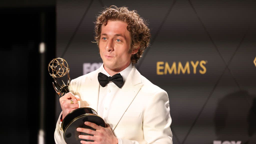 jeremy allen white holds an emmy trophy and looks left, he wears a white tuxedo with a black bowtie