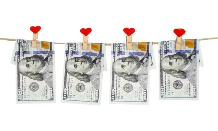 $100 bills hung on a string by close pins with a heart on them.