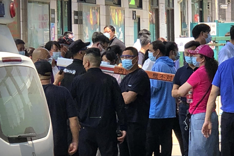 Police and security officials watch as people gather at a coronavirus testing center at a sports facility in Beijing, Tuesday, June 16, 2020. China reported several dozen more coronavirus infections Tuesday as it increased testing and lockdown measures in parts of the capital to control what appeared to be its largest outbreak in more than two months. (AP Photo/Mark Schiefelbein)