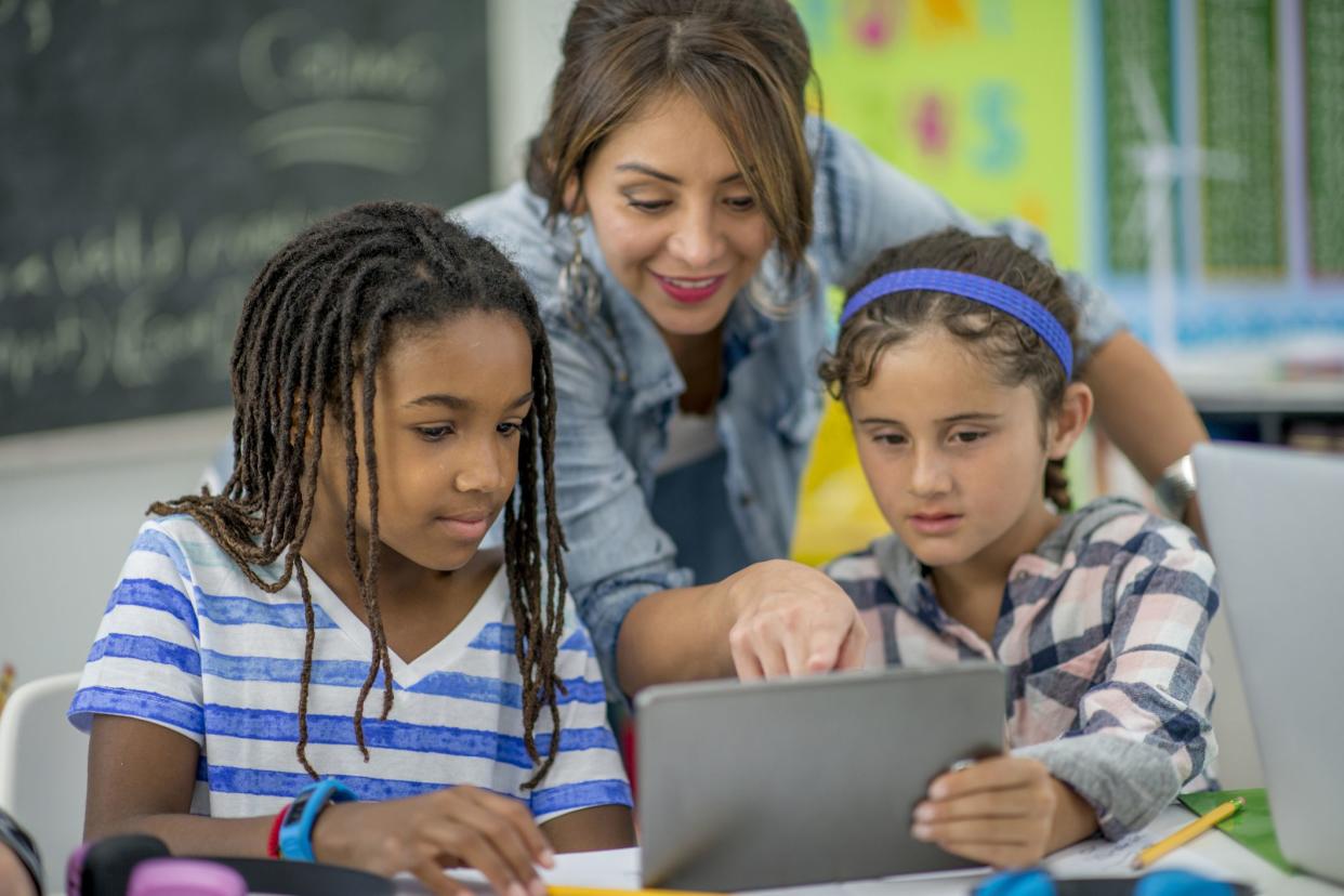 teacher helping students working with tablet in classroom