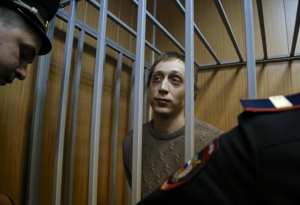 Pavel Dmitrichenko looks through bars as he stands in a cage at a court room in Moscow on Tuesday, Oct. 22, 2013. Bolshoi dancer Dmitrichenko goes on trial on Tuesday, on charges of organizing an acid attack against the ballet's artistic director, Sergei Filin. (AP Photo/Alexander Zemlianichenko)